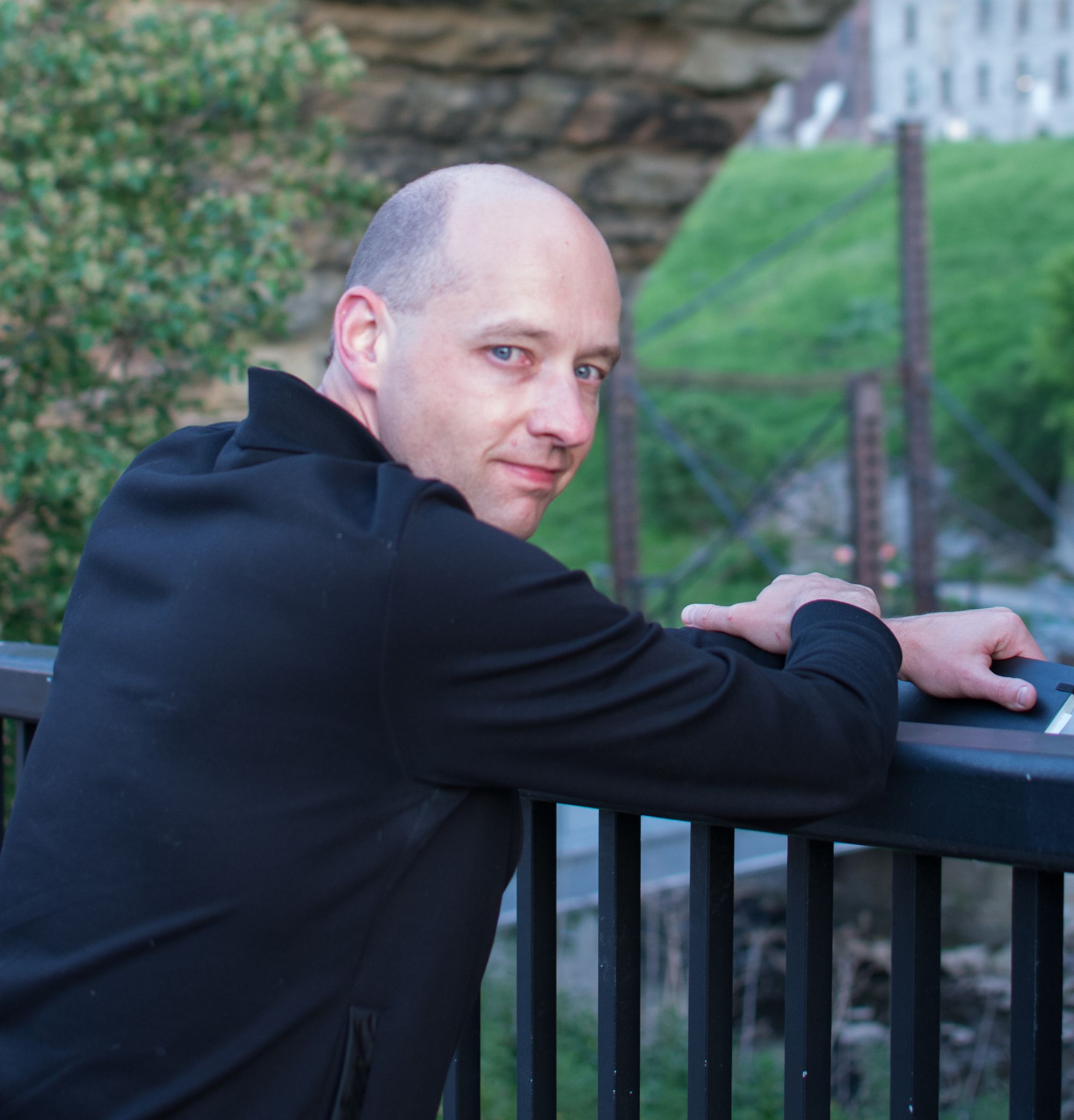 Steffen looking over shoulder at camera while leaning on railing overlooking park and industrial landscape